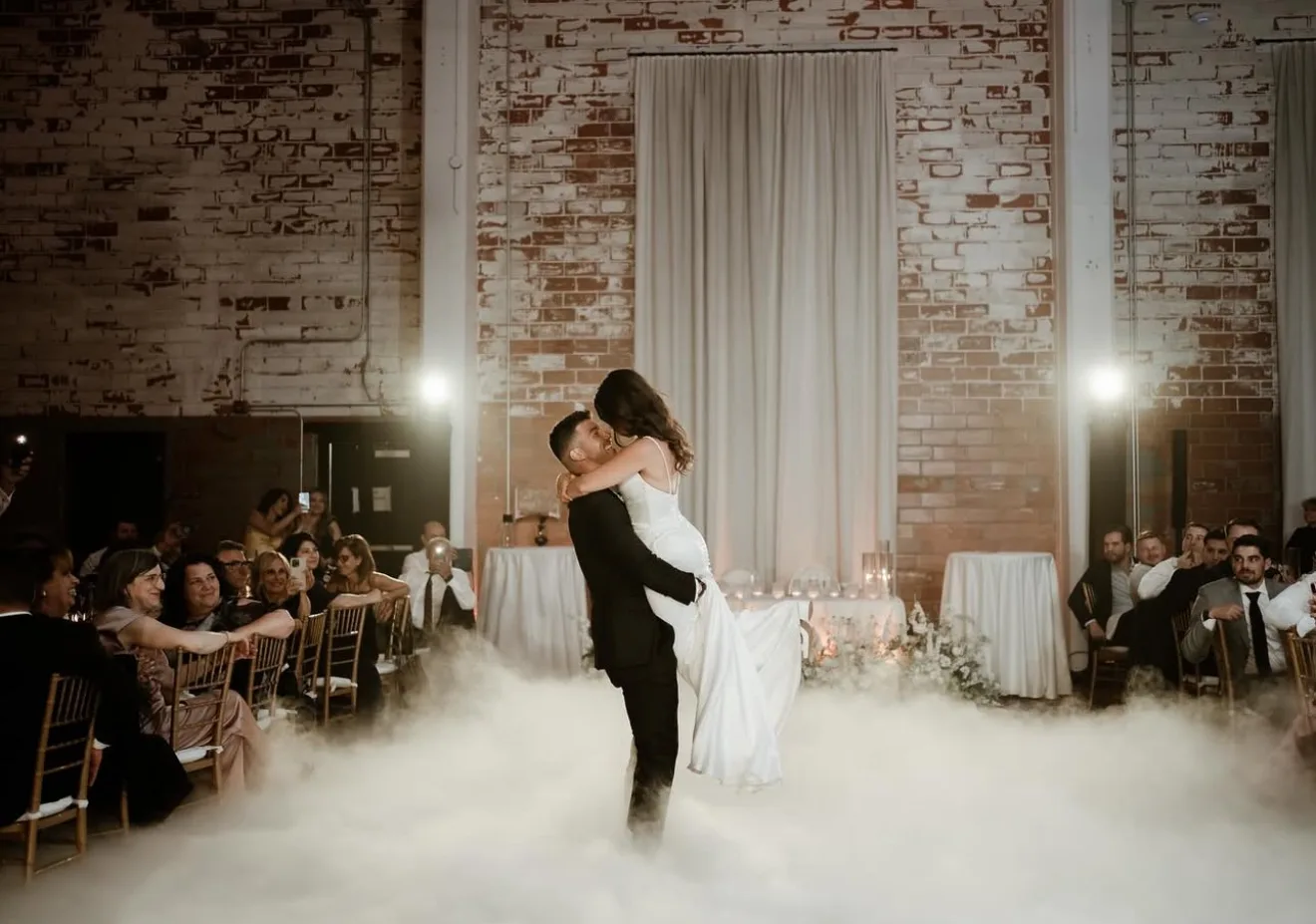 Couple lifted mid first dance inside a low cloud of dry ice