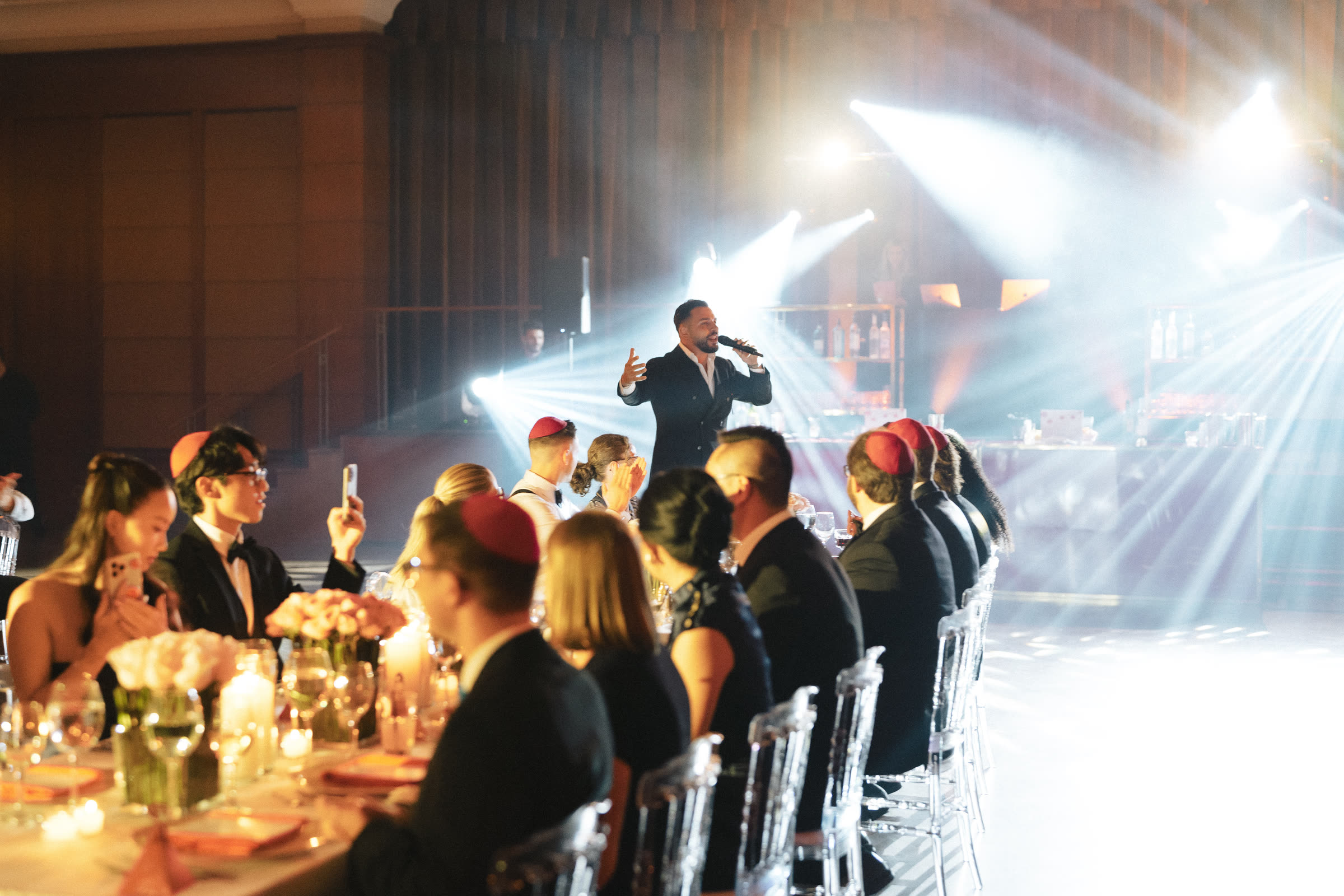 Majd MCing on a wireless microphone at a seated dinner