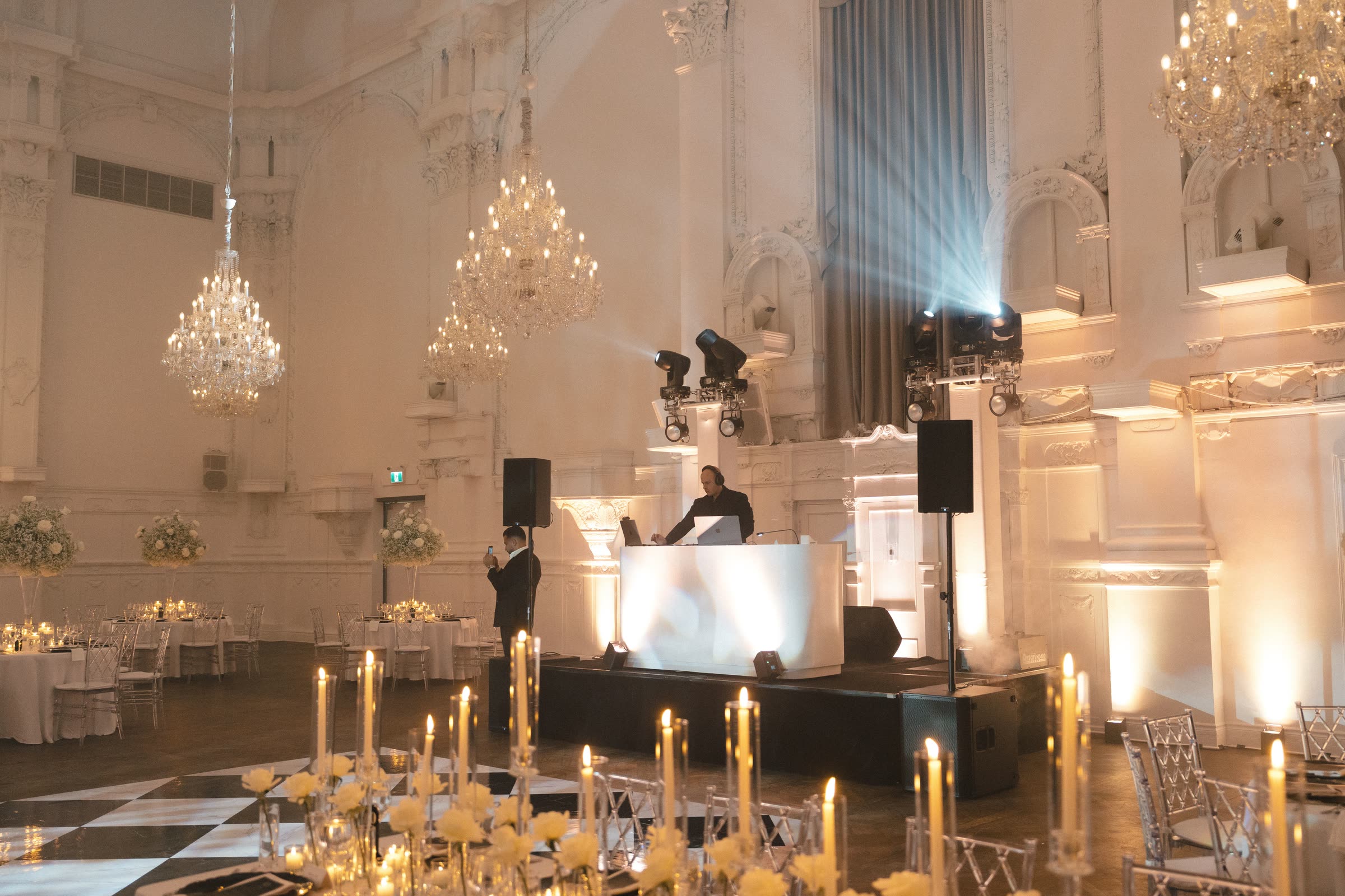 White DJ booth and uplighting set cleanly into a chandeliered ballroom