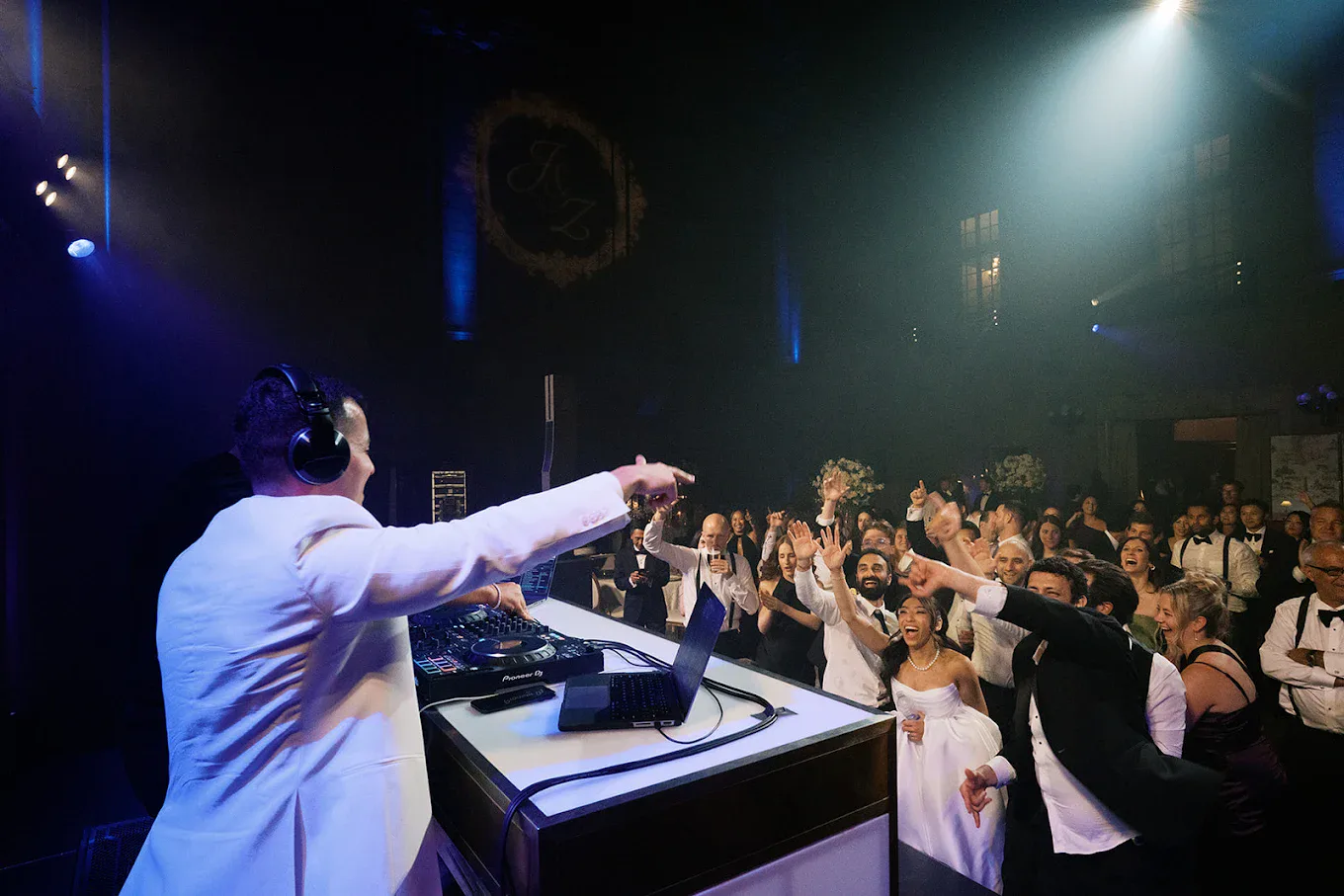 DJ in a white tuxedo facing the crowd under the couple’s monogram at Théâtre St-James
