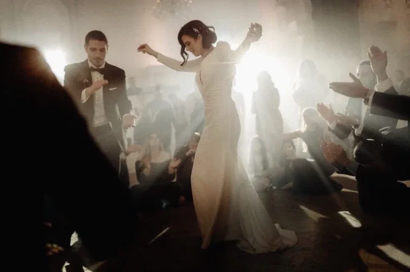 Bride dancing in a backlit haze as guests clap around the floor